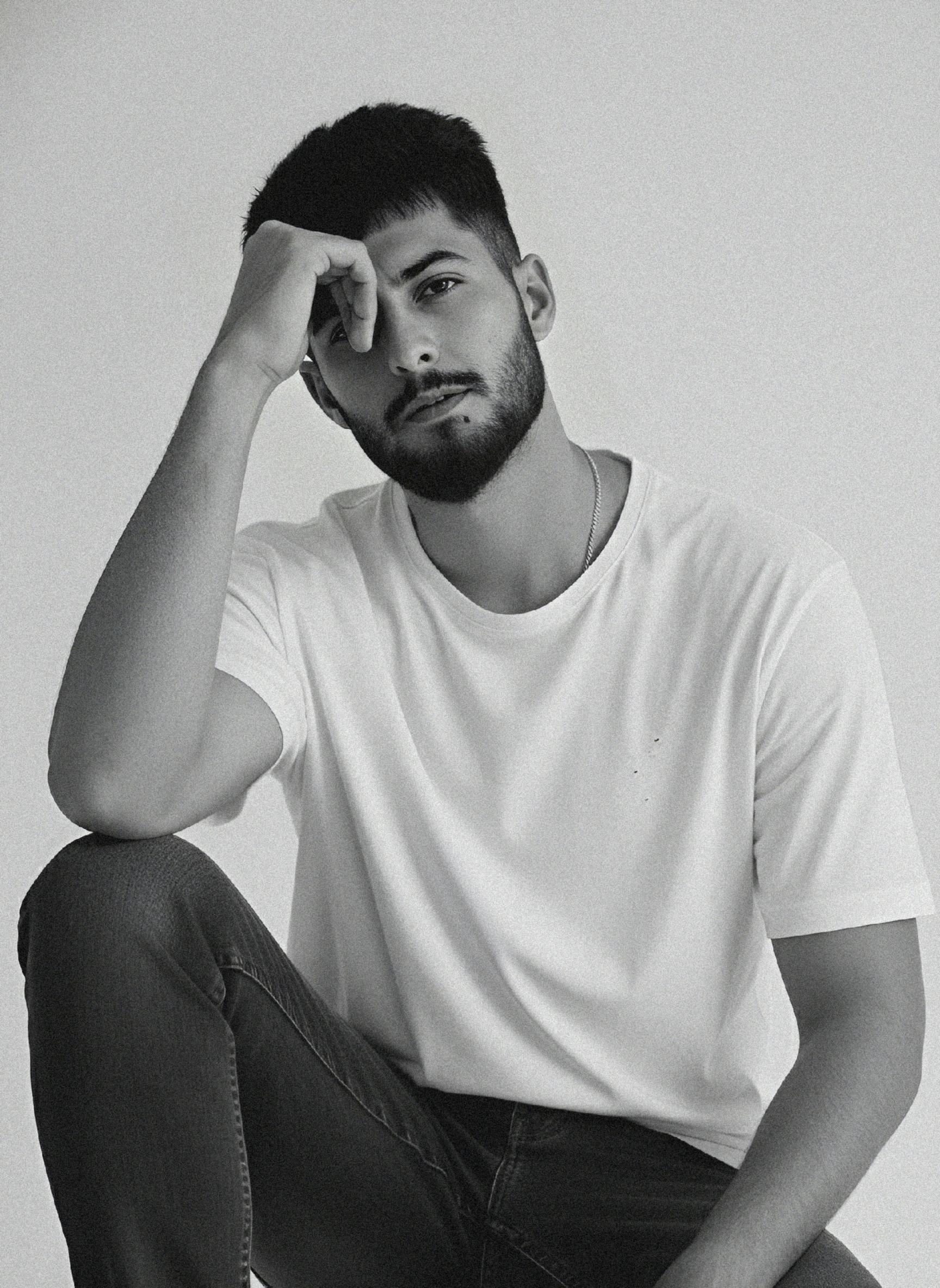 A man with dark hair and beard contemplating.